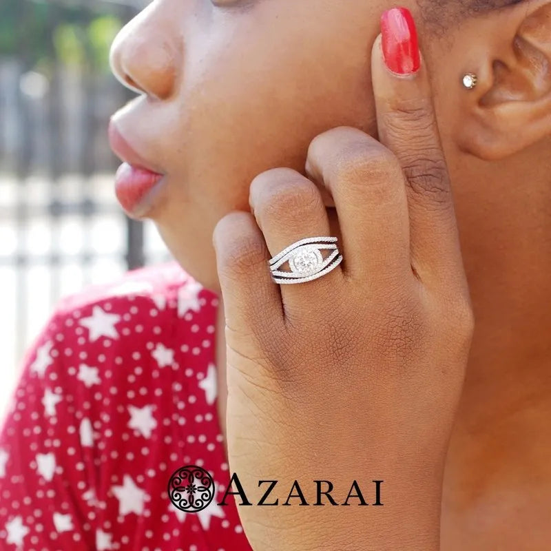 A person wearing a red patterned shirt showcases the exquisite Raquel sterling silver bridal set, highlighting a diamond ring with multiple bands on their finger. The name "AZARAI" is prominently displayed at the bottom, suggesting exclusive craftsmanship in sterling silver.