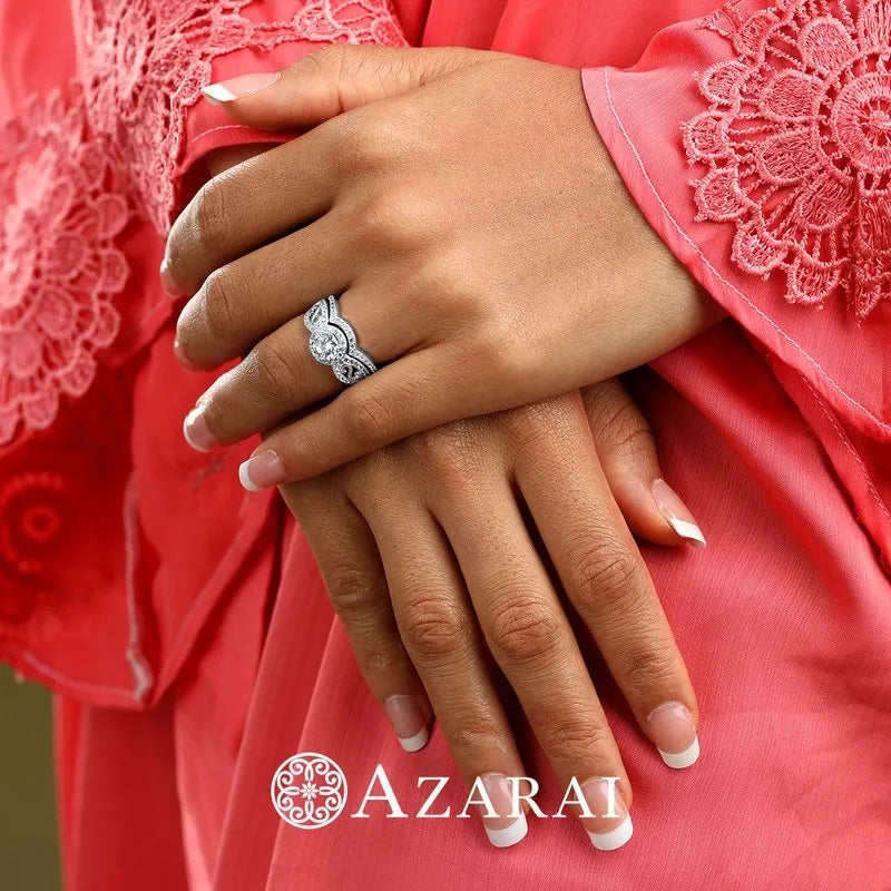 Close-up of a person wearing a pink lace garment, with manicured hands adorned with the Miele sterling silver bridal set and two rings, one featuring a central gemstone. The Azarai logo is visible at the bottom.