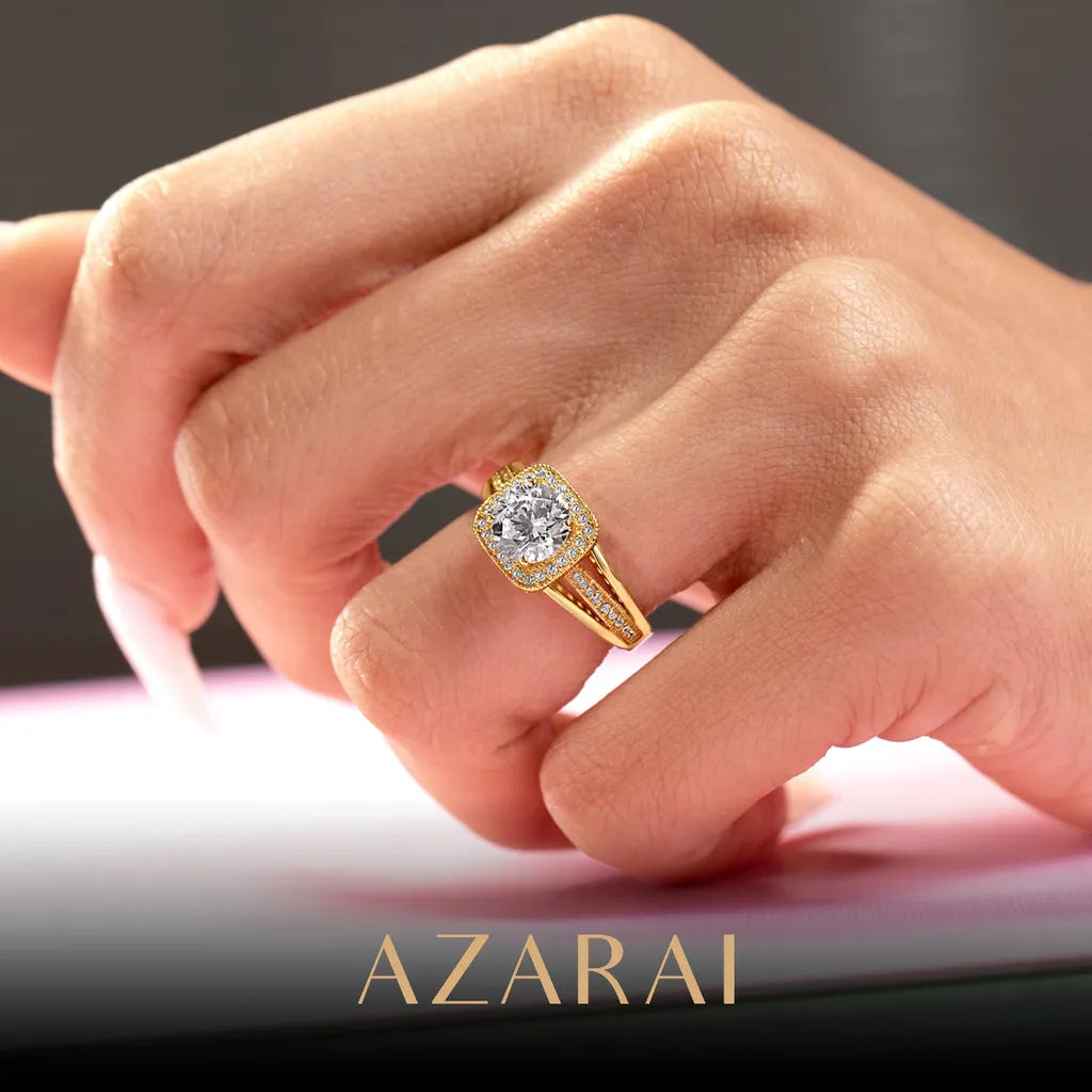 A hand with manicured nails, showcasing an Eloise 14kt gold engagement ring embellished with diamonds, is elegantly displayed against a pink background, with "AZARAI" inscribed at the bottom.