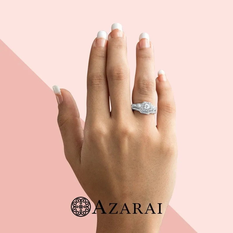 A hand adorned with the Amelia sterling silver bridal set, showcasing a central diamond and smaller stones, elegantly against a pink background. The Azarai logo adorns the bottom, enhancing the allure of this exquisite piece.