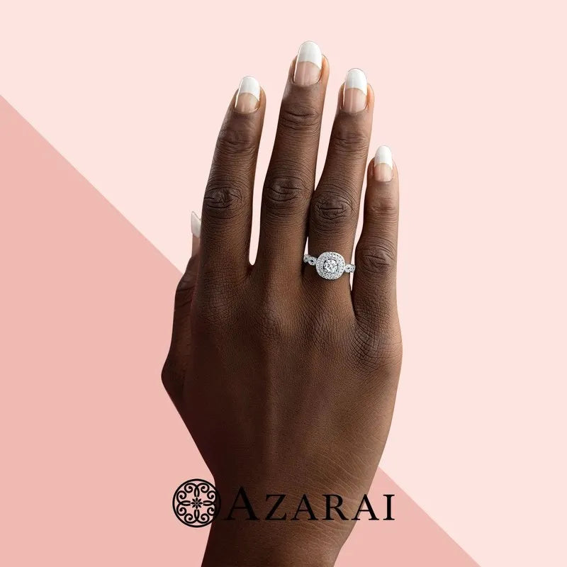 A hand adorned with the elegant Astrid sterling silver engagement ring on the ring finger is showcased against a pink background, with the "Azarai" logo subtly resting at the bottom.