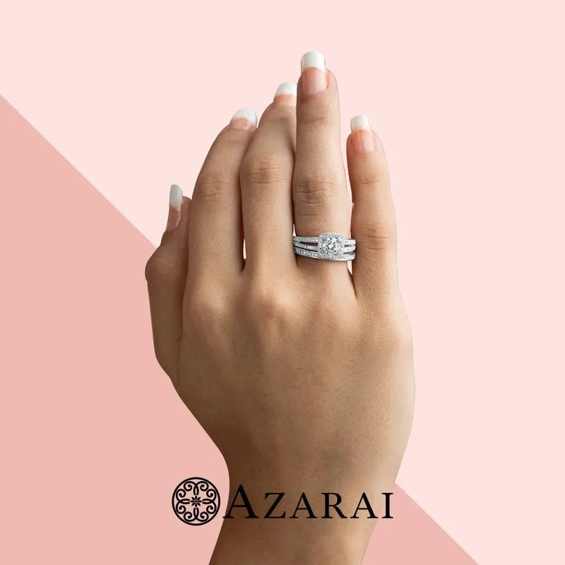 A hand with manicured nails showcases an elegant Eva sterling silver bridal set ON CLEARANCE, featuring a diamond engagement ring and wedding band. The background is pink with the text "AZARAI" and a circular design logo at the bottom.