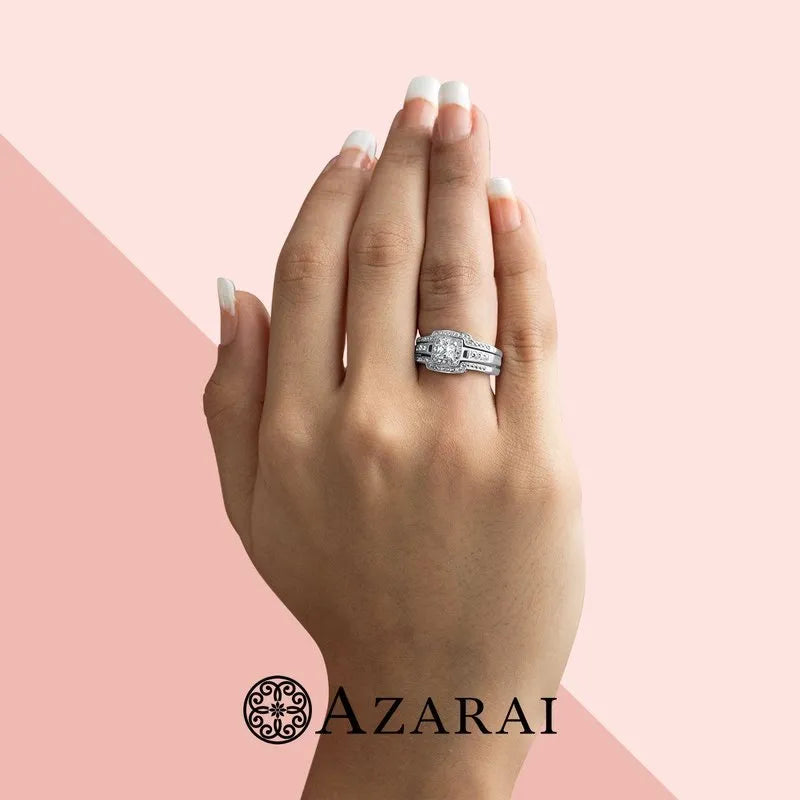 Against a pink and beige backdrop featuring the Azarai logo, a hand with a polished manicure showcases a sterling silver diamond ring from the Henriette bridal set, now on clearance.