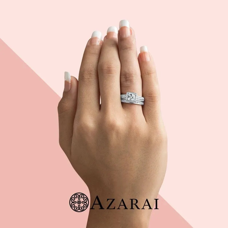 A manicured hand showcases the Hepburn sterling silver bridal set ON CLEARANCE, with a dazzling diamond ring against a pink background, and the "AZARAI" logo elegantly placed at the bottom.