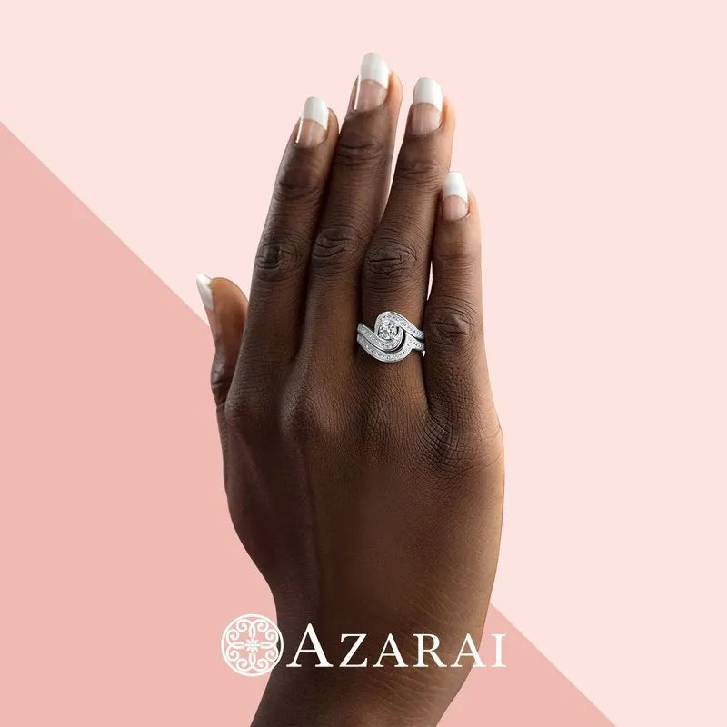 A hand with manicured nails elegantly displays the Katrina sterling silver bridal set, now on clearance. The backdrop features a split pink design with the text "AZARAI" and a decorative circle logo below, evoking a sense of grace that perfectly complements this enchanting collection.