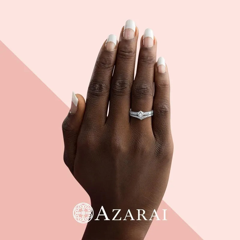 A hand adorned with a sparkling diamond ring from the Sofia Sterling Silver bridal set is set against a pink and peach background, showcasing its elegance, with the "AZARAI" logo elegantly placed at the bottom.