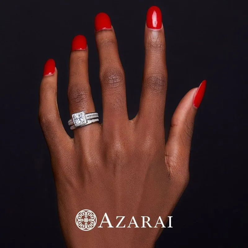 A hand with red nail polish wears a dazzling Hepburn sterling silver bridal ring set, displayed against a black background. The word "AZARAI" elegantly appears at the bottom.