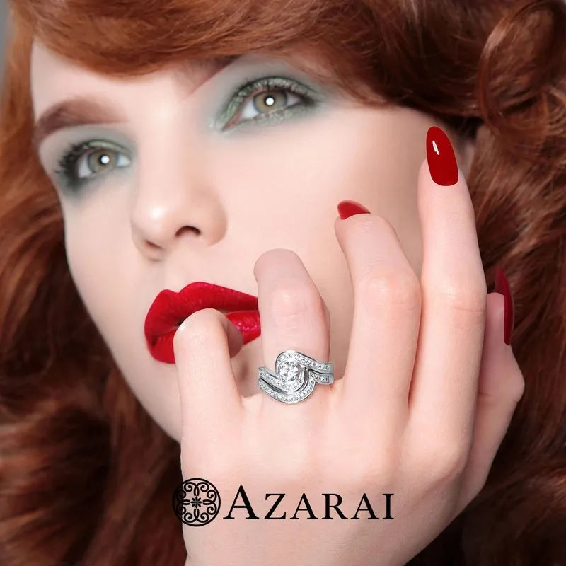 A woman with vibrant red hair and nails elegantly displays a large Katrina sterling silver bridal set from the Azarai collection, currently on clearance. Her makeup accentuates her striking style, with bold red lipstick and green eyeshadow, while the "Azarai" logo at the bottom of the image adds an elegant touch to this look.