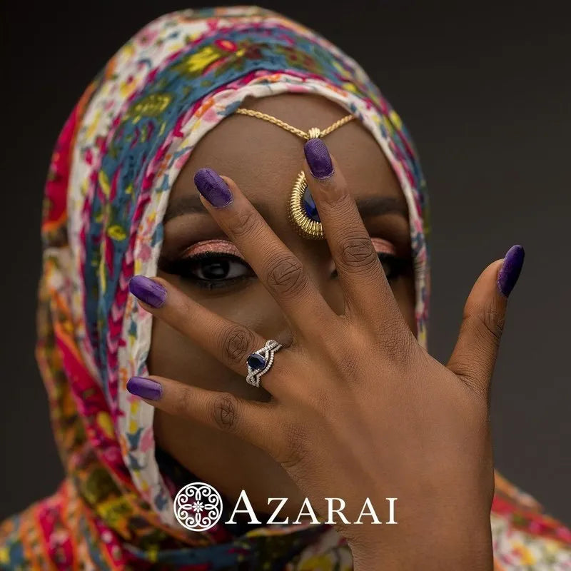 A woman adorned in a vibrant hijab and jewelry conceals part of her face with her hand, showcasing purple nail polish and rings. One of the rings is the exquisite Adelaide sterling silver bridal set. The name "AZARAI" is visible at the bottom.