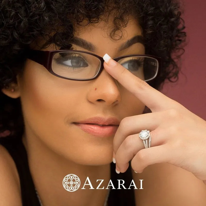 A woman with curly hair and glasses adjusts her frames, flaunting a dazzling diamond ring from the Britney sterling silver bridal set ON CLEARANCE. The discreet "AZARAI" logo at the bottom hints at the elegance within an Azarai ring box.