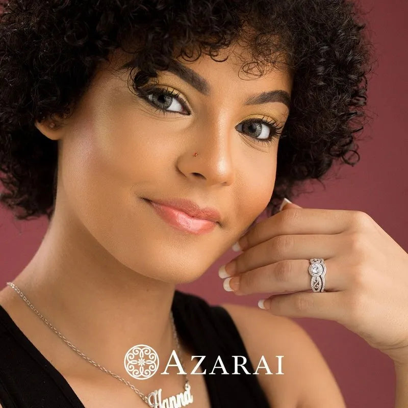 A person with curly hair proudly showcases the Miele sterling silver bridal set on their left hand against a vivid red background, with the Azarai logo subtly visible.