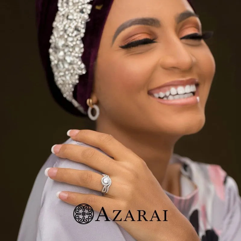 A smiling person adorned with a jeweled headscarf and shimmering diamond rings elegantly cradles their face. A sterling silver "Lianne" bridal set from AZARAI gracefully enhances the scene, adding a touch of elegance to this radiant moment.