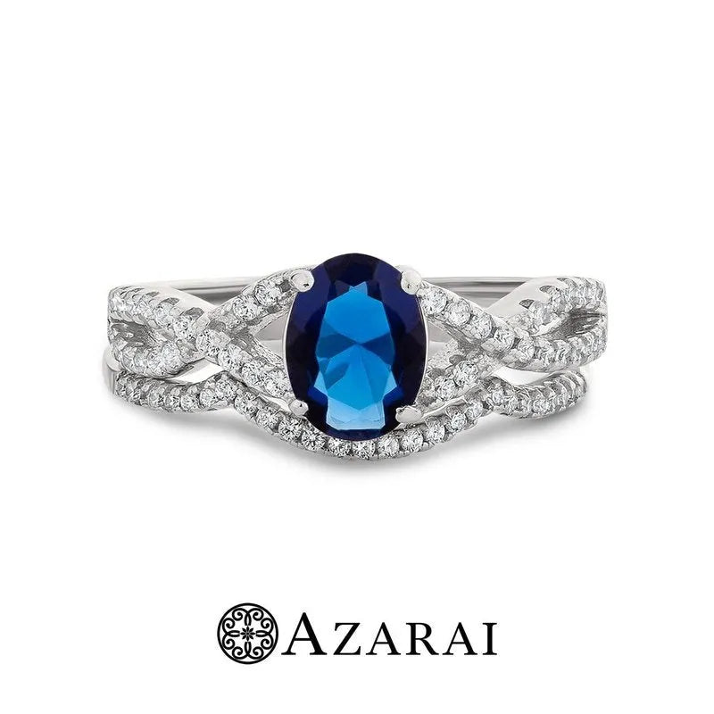 The Adelaide sterling silver bridal set features a stunning blue oval gemstone at its center, surrounded by small clear stones, making it an exquisite choice for a bridal ring. The word "AZARAI" is elegantly displayed below the ring.