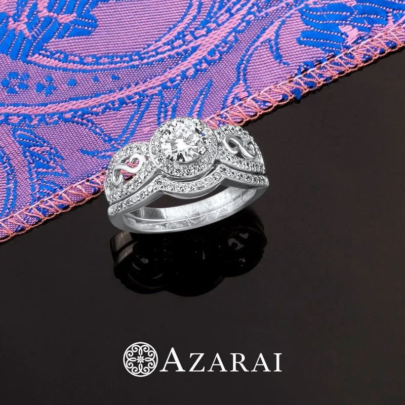 The Miele sterling silver bridal set, featuring intricate designs and a prominent central diamond, rests on a black surface, enhanced by a purple patterned cloth in the background. The word "AZARAI" is elegantly inscribed at the bottom.