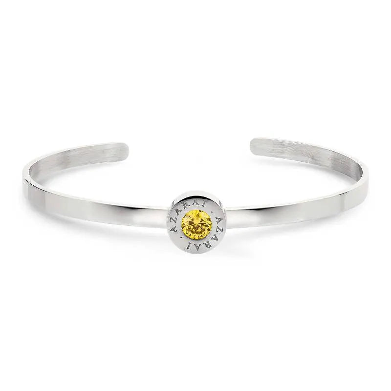 The Varia birthstone women's bracelet showcases a stunning silver design with a round yellow gemstone as the centerpiece, elegantly engraved with "AZARAI" around the stone. It is an ideal choice for a personalized birthstone bracelet, exuding elegance and style.