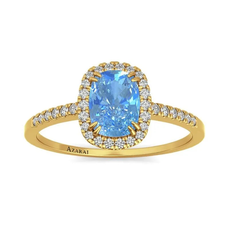 The Adeline 9kt gold engagement ring showcases a luxurious band adorned with diamonds. At its centerpiece is a breathtaking cushion-cut blue gemstone, beautifully surrounded by delicate sparkling diamonds, embodying an everlasting symbol of love and commitment.