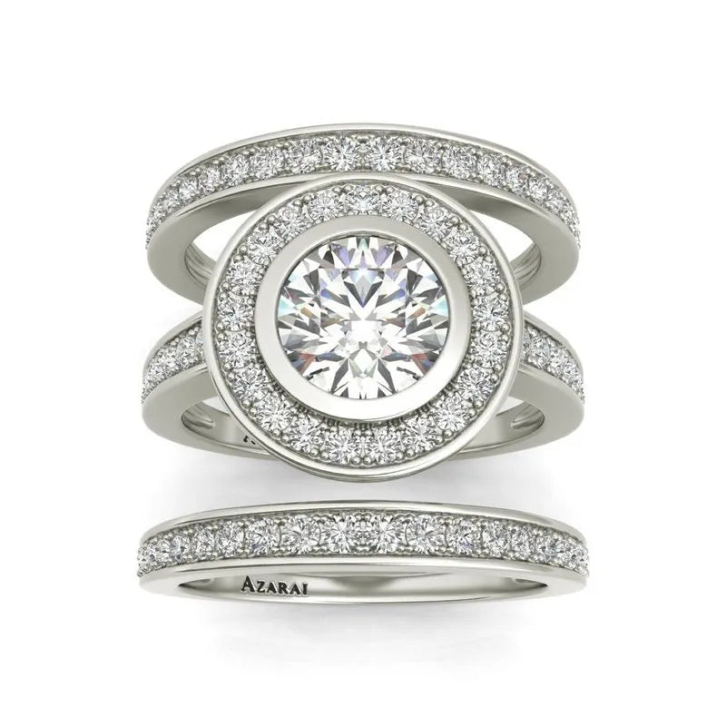 The Chamise sterling silver bridal set, currently on clearance, showcases a large round diamond at the center surrounded by smaller diamonds and features a split band encrusted with diamonds, making it an exquisite addition to any bridal ensemble.