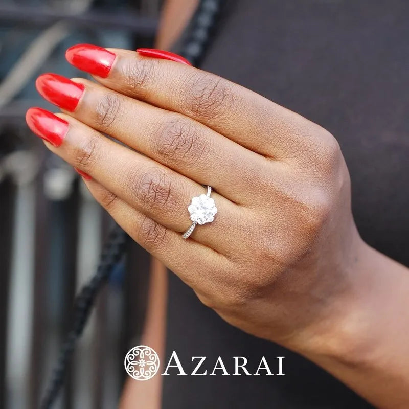 A hand with red nails showcases the stunning Charlotte sterling silver engagement ring featuring a large, round diamond. The word "AZARAI" is printed at the bottom, indicating it's on clearance.