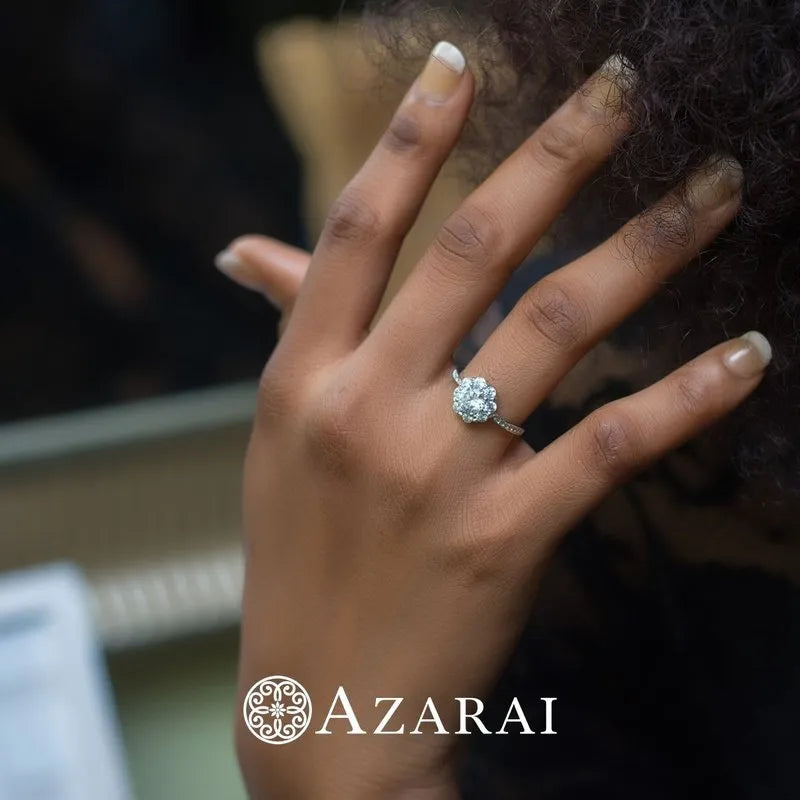 A hand adorned with the Charlotte sterling silver engagement ring, showcasing a large gemstone, is set against a dark background. The brand name "Azarai" appears in the lower corner, indicating this exclusive piece is likely part of their clearance selection.