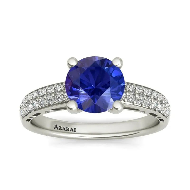 A Dakota sterling silver engagement ring, currently on clearance, showcases a large blue gemstone at its center, adorned with small clear stones along the band. The word "Azarai" is elegantly engraved inside, making it an ideal choice for the modern bride seeking elegance.