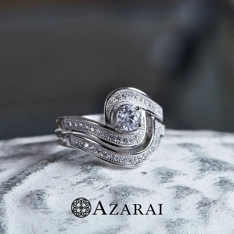 The Katrina sterling silver bridal set, now on clearance, features an intricate ring with a central diamond set on a textured surface, complete with the Azarai logo below. Perfect for a bridal collection.