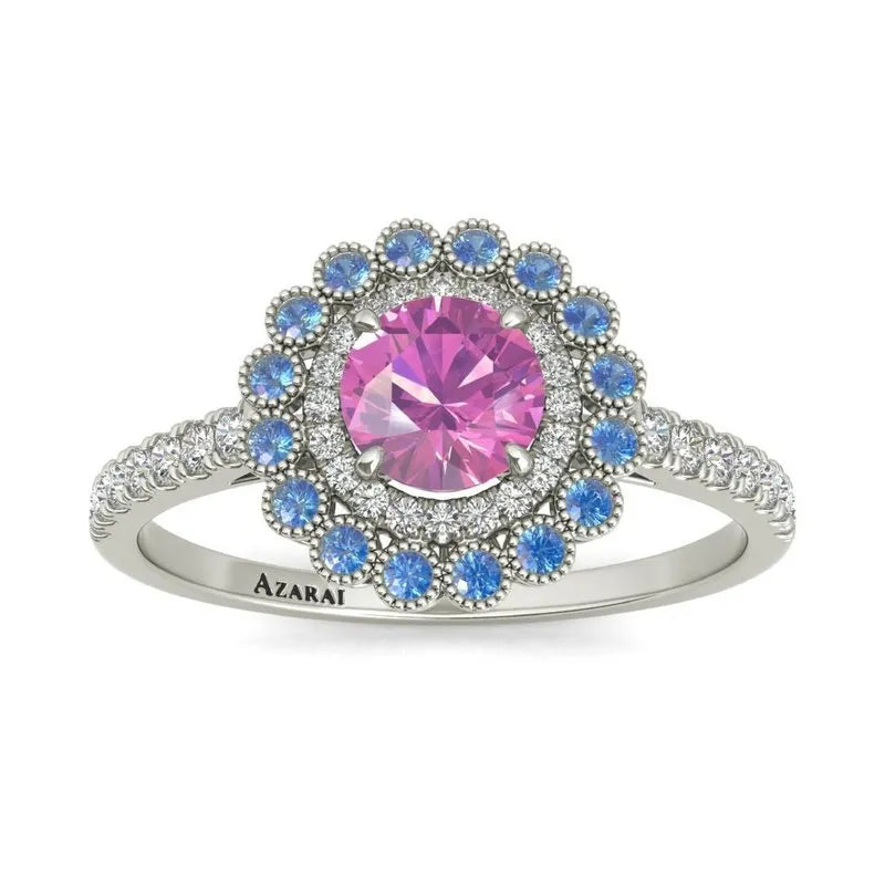 This exquisite Portia 9kt gold engagement ring features a striking large pink center stone encircled by smaller blue stones, complemented by clear stones along the band. Crafted from stunning 9kt gold, this ring offers a distinctive expression of love and commitment.