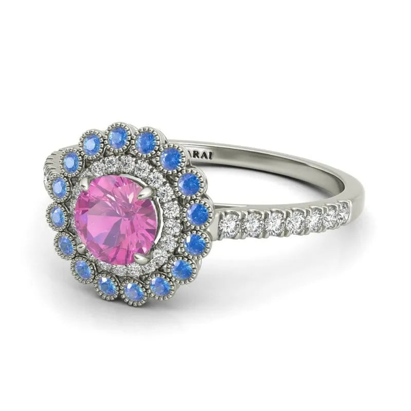 The Portia 9kt gold engagement ring showcases a pink center stone, beautifully complemented by small blue stones and clear stones on its elegant band.