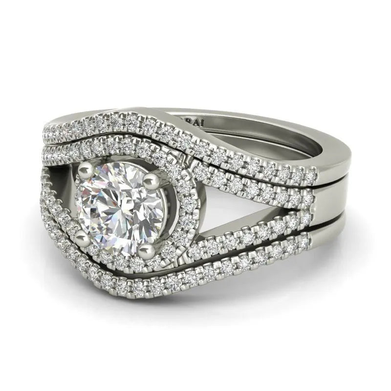 The Raquel sterling silver bridal set, currently on clearance, showcases a breathtaking engagement ring with a large round diamond at its center. It is gracefully encircled by two layers of smaller diamonds on a dual band.