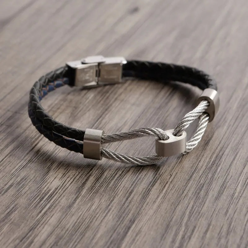 The Volte leather and stainless steel men's bracelet, featuring a silver cable and sleek clasp detail, rests elegantly on a wooden surface.